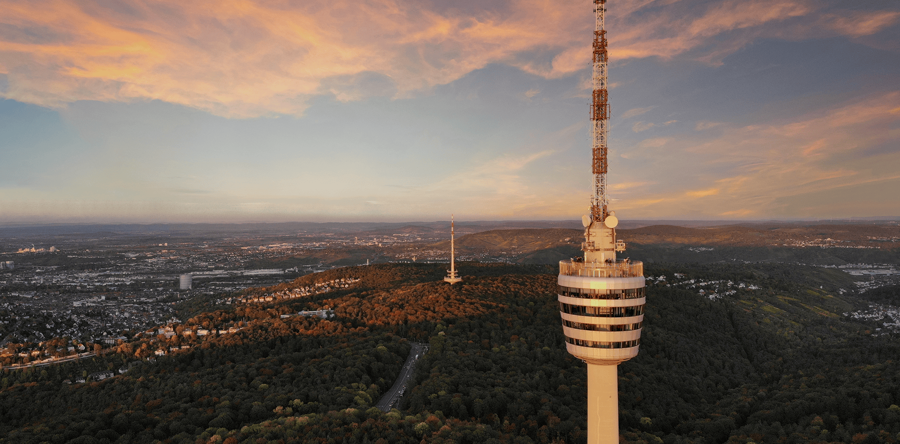 Drohnenaufnahme von Stuttgart mit dem Fernsehturm im Vordergrund, bei Sonnenuntergang.